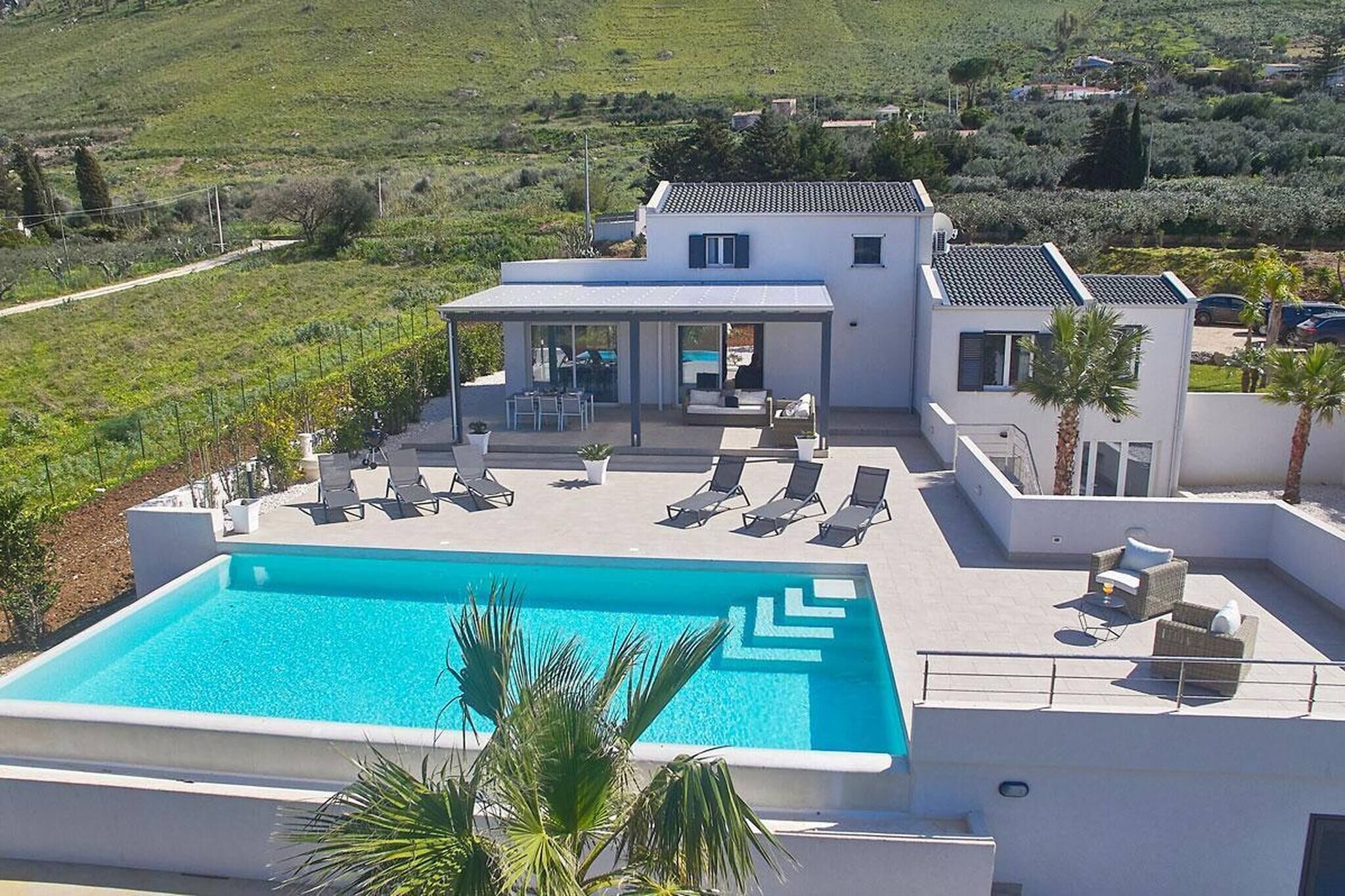 Eine moderne Villa mit Schwimmbad, Liegestühlen und einer überdachten Terrasse.
