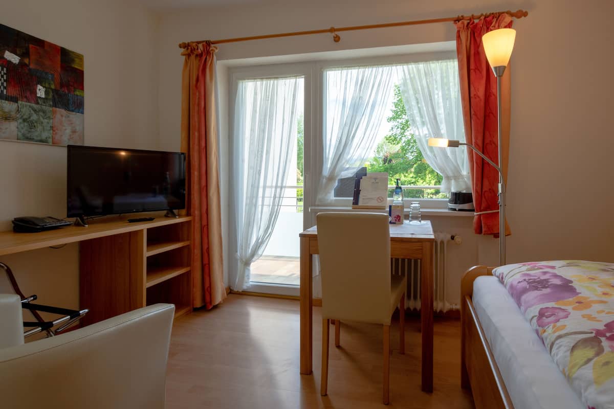 Une chambre avec un lit, un bureau, une chaise, une télévision et une fenêtre avec des rideaux.