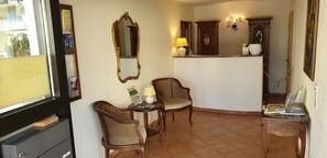 A room with two wicker chairs, a small table with a lamp, a mirror, and a wooden cabinet. - Casa Cristina- Kurpension und Appartements (Bad Krozingen)