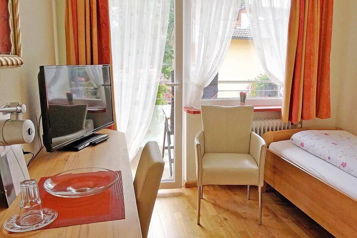 Une petite chambre d’hôtel avec un lit simple, un bureau avec une télévision, une chaise et une fenêtre avec des rideaux.