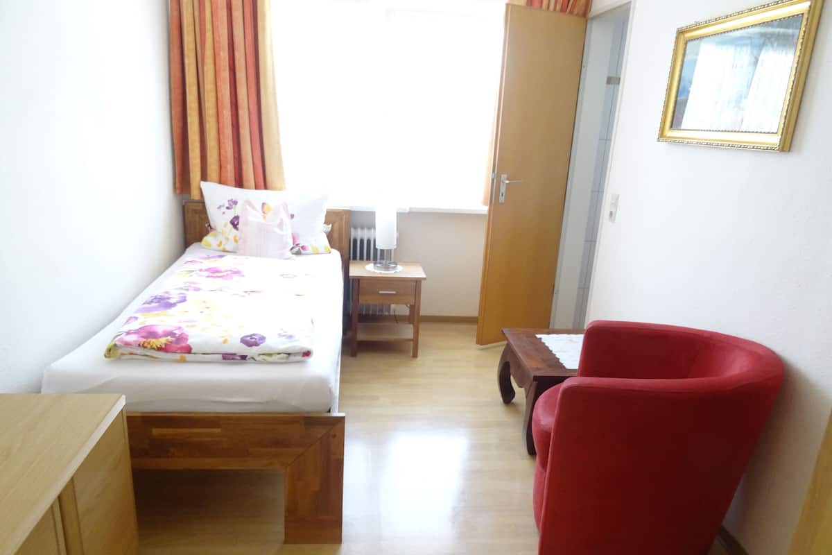 Une chambre à coucher avec un lit, une table de chevet en bois, une chaise rouge et une armoire en bois.