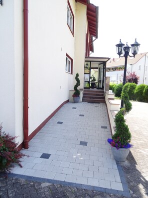 A building entrance with a paved walkway, potted plants, and a visible door. - Casa Cristina- Kurpension und Appartements (Bad Krozingen)