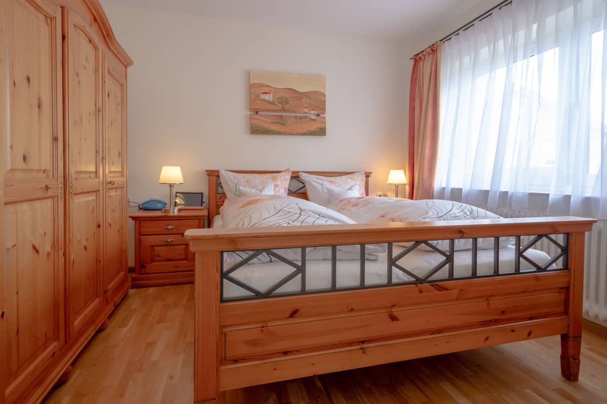 Un lit en bois avec une tête de lit en verre, deux tables de chevet, une petite table et une armoire.