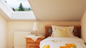 Ein Schlafzimmer mit Oberlicht, einem Holznachttisch, einer Lampe, einer Heizung und einem Bett mit floralem Bettzeug.
