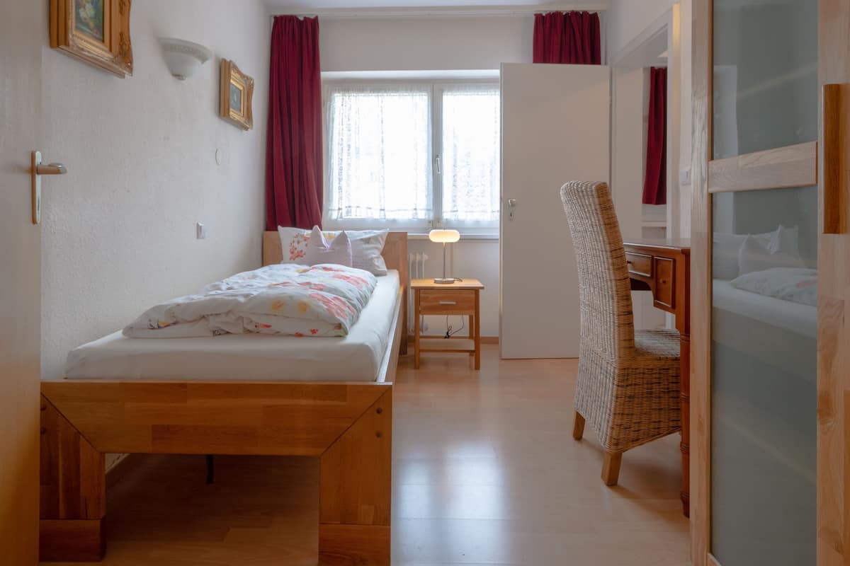 Une chambre à coucher avec un lit, une chaise, un bureau et une fenêtre avec des rideaux.