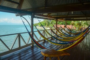 Una terraza de madera con una hamaca y una silla con vista a un cuerpo de agua.