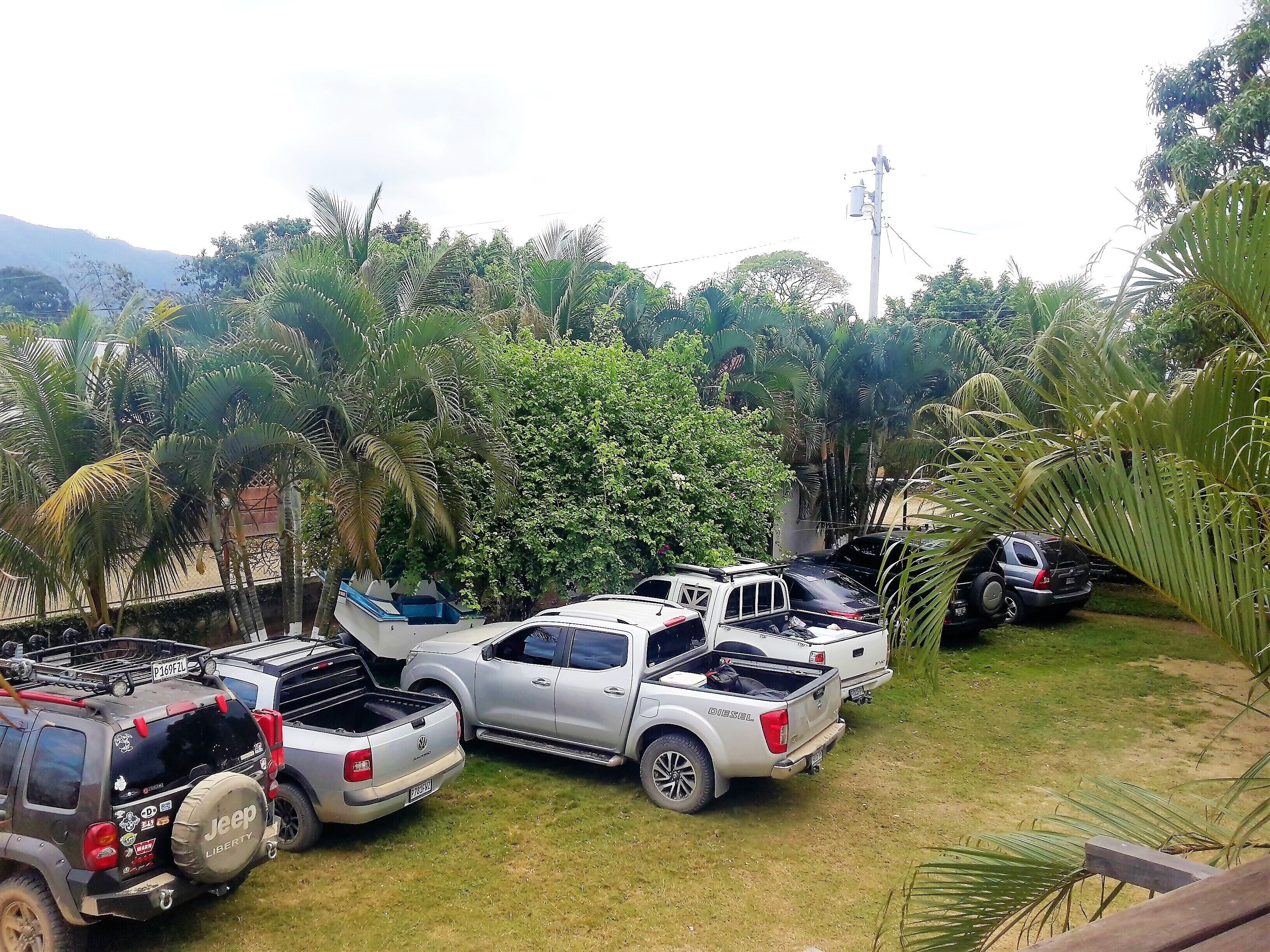 A parking area with several pickup trucks, surrounded by lush greenery and palm trees.