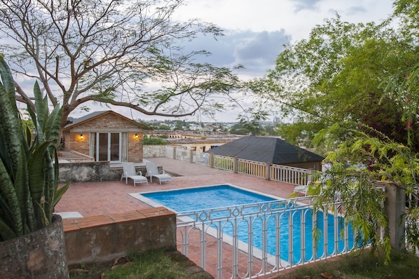 Relax in a serene backyard with a swimming pool, surrounded by lush greenery and a cozy brick building.