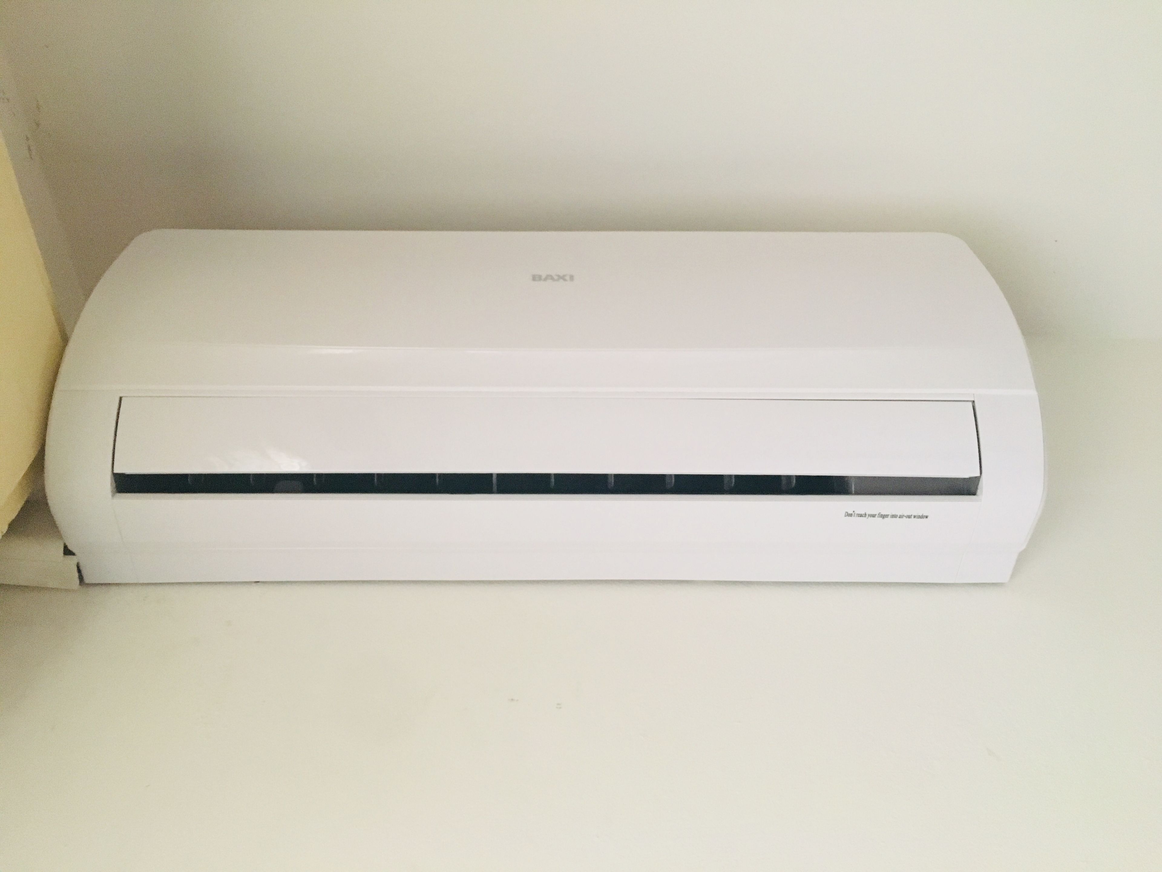 A white wall-mounted air conditioning unit with a control panel and a warning label.