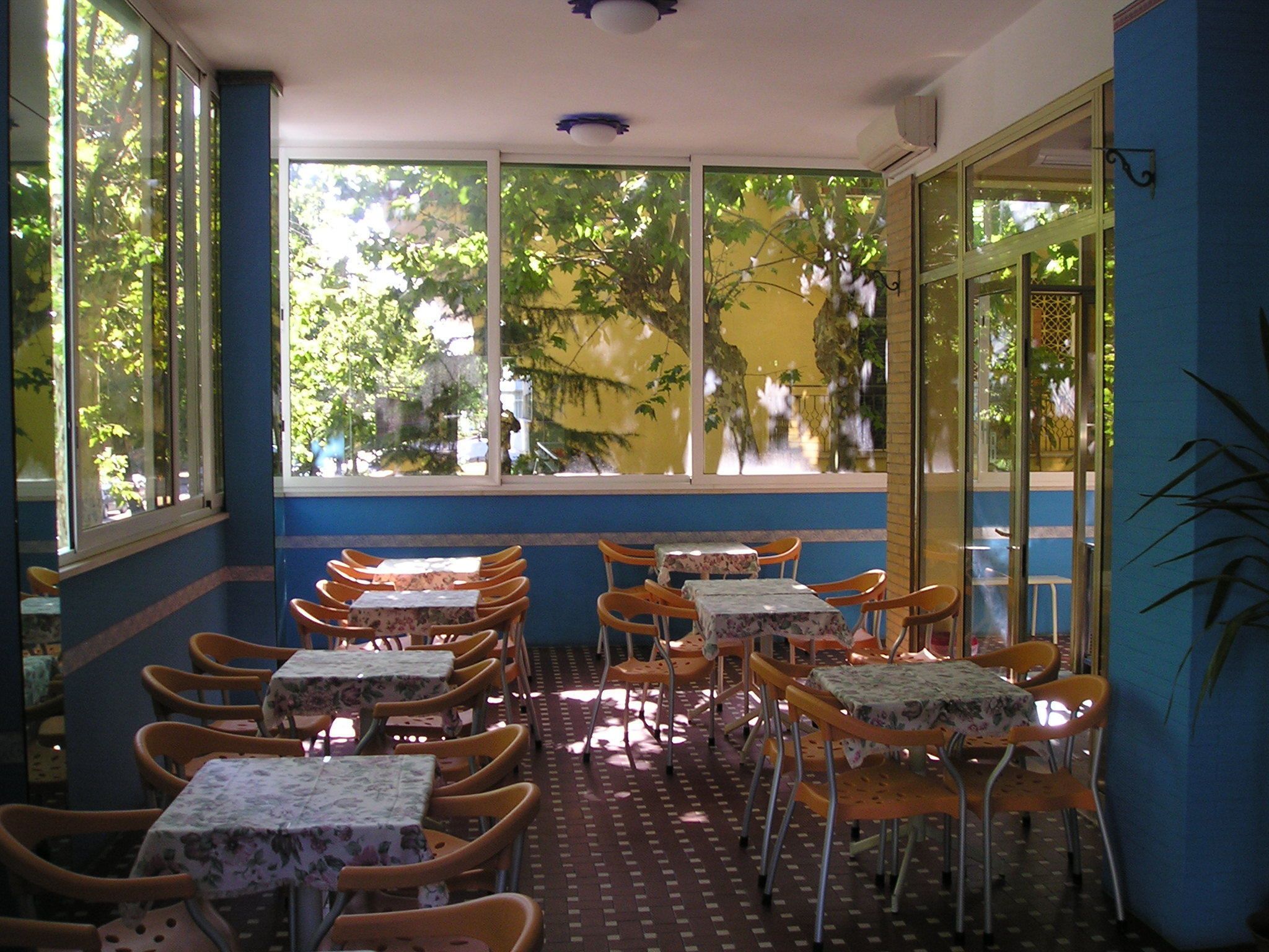 An indoor dining area with tables and chairs, large windows with views of trees, and a patterned floor.