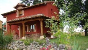 Una casa roja con fachada de piedra, un porche y un pequeño estanque con rocas y flores.