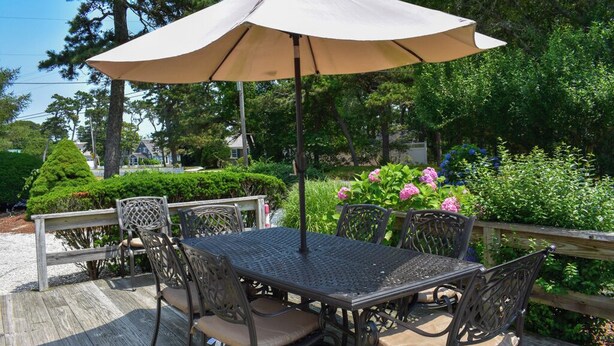 Una terraza con mesa y sillas, rodeada por una barandilla de madera, y una sombrilla grande proporcionando sombra.