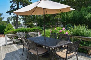 Eine Terrasse mit Tisch und Stühlen, umgeben von einem Holgitter, und ein großer Sonnenschirm spendet Schatten.