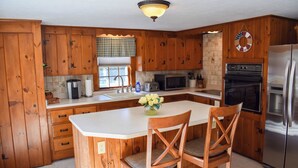 Una cocina con armarios de madera, encimera blanca, refrigerador de acero inoxidable y microondas.