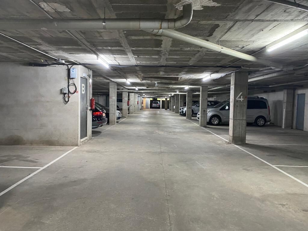 A multi-level parking garage with concrete floors and pillars, several cars parked, and emergency equipment visible.