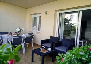 A balcony with a dining table set for two, a sofa, and a small table with food. - Stil Mar Anna Terra - Apartment with Garden & Pool (L'Escala)