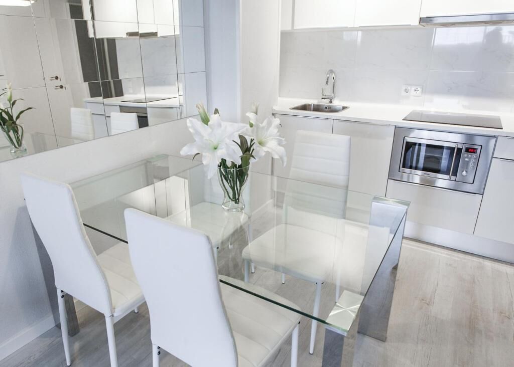 A modern kitchen with a glass dining table, white chairs, a stainless steel microwave, and a sink.