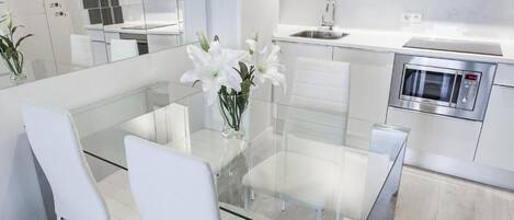 A modern kitchen with a glass dining table, white chairs, a stainless steel microwave, and a sink.