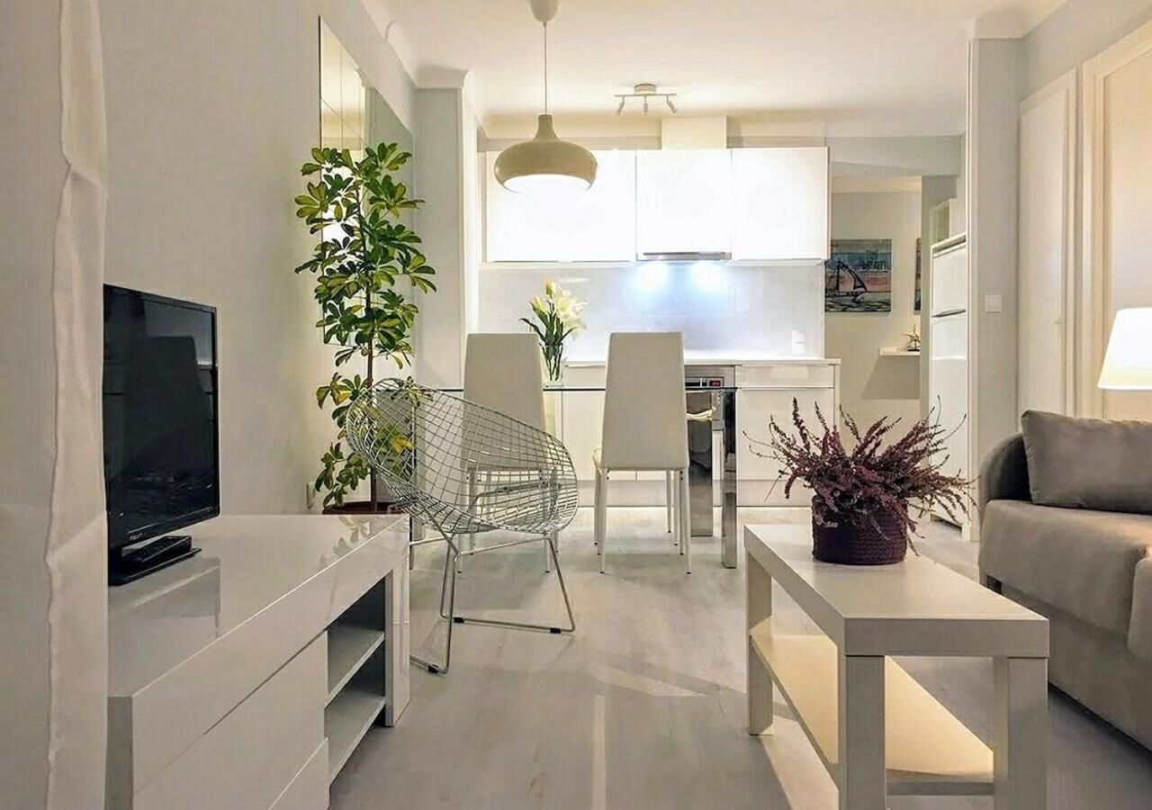 Een moderne woonkamer met een flatscreen televisie, een metalen stoel, een eettafel met stoelen, een bank en een keuken op de achtergrond.