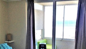 Een hotelkamer met een bed, een stoel, een klein tafeltje en uitzicht op de oceaan door een schuifdeur.