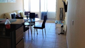Een woonkamer met een bank, een eettafel met stoelen en een keukenhoek met een aanrecht en kastjes.