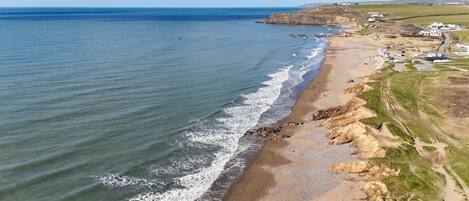 An aerial view of a coastal area with a beach, cliffs, and a small settlement.
