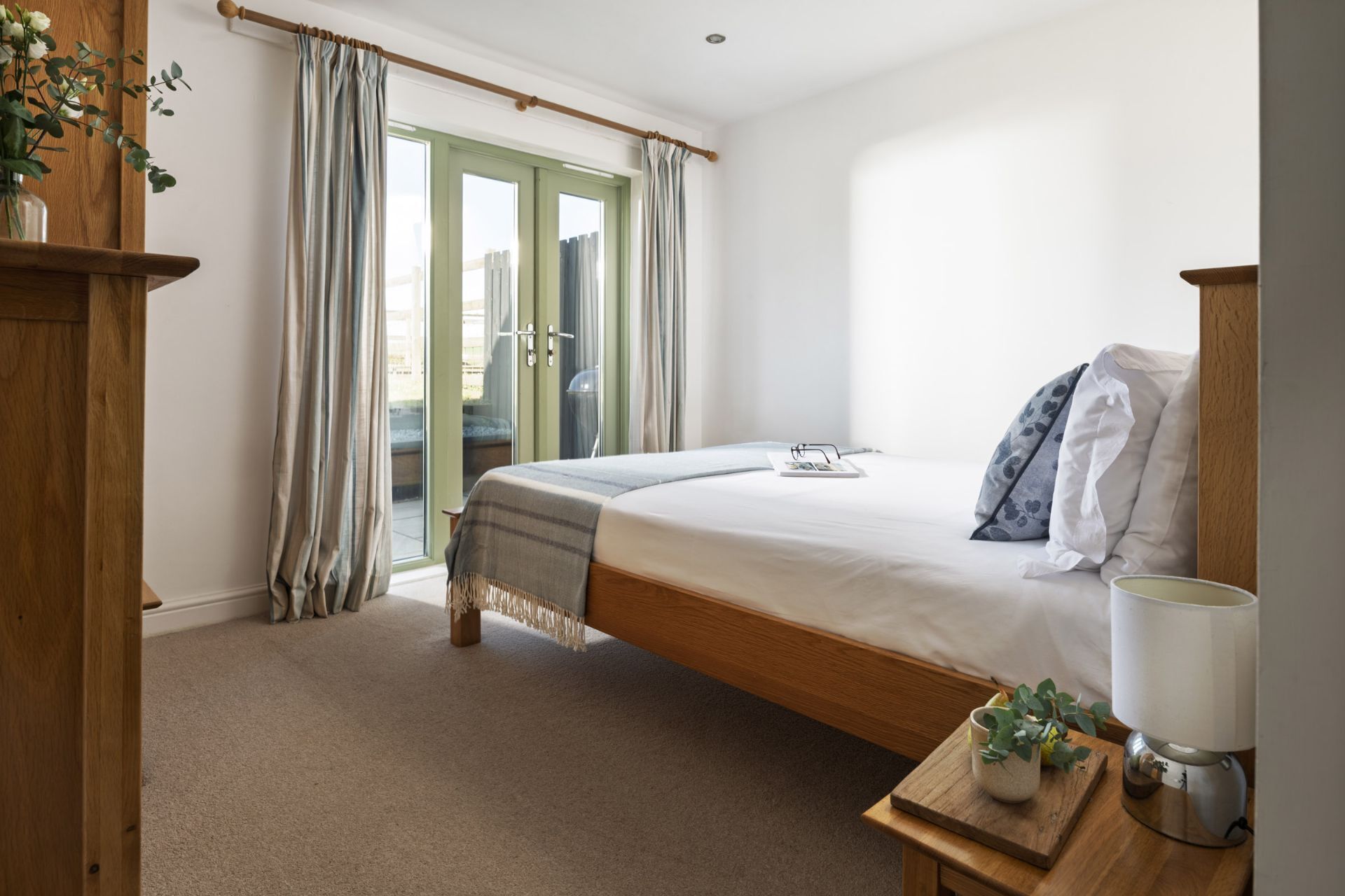 Une chambre à coucher avec un lit, une table de chevet avec une lampe, une fenêtre avec des rideaux et une vue sur l’extérieur.