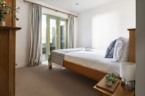 Un dormitorio con cama, mesita de noche con lámpara, ventana con cortinas y vistas al exterior.