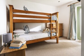 A bunk bed with a desk and lamp, a wooden dresser, and a window with curtains.
