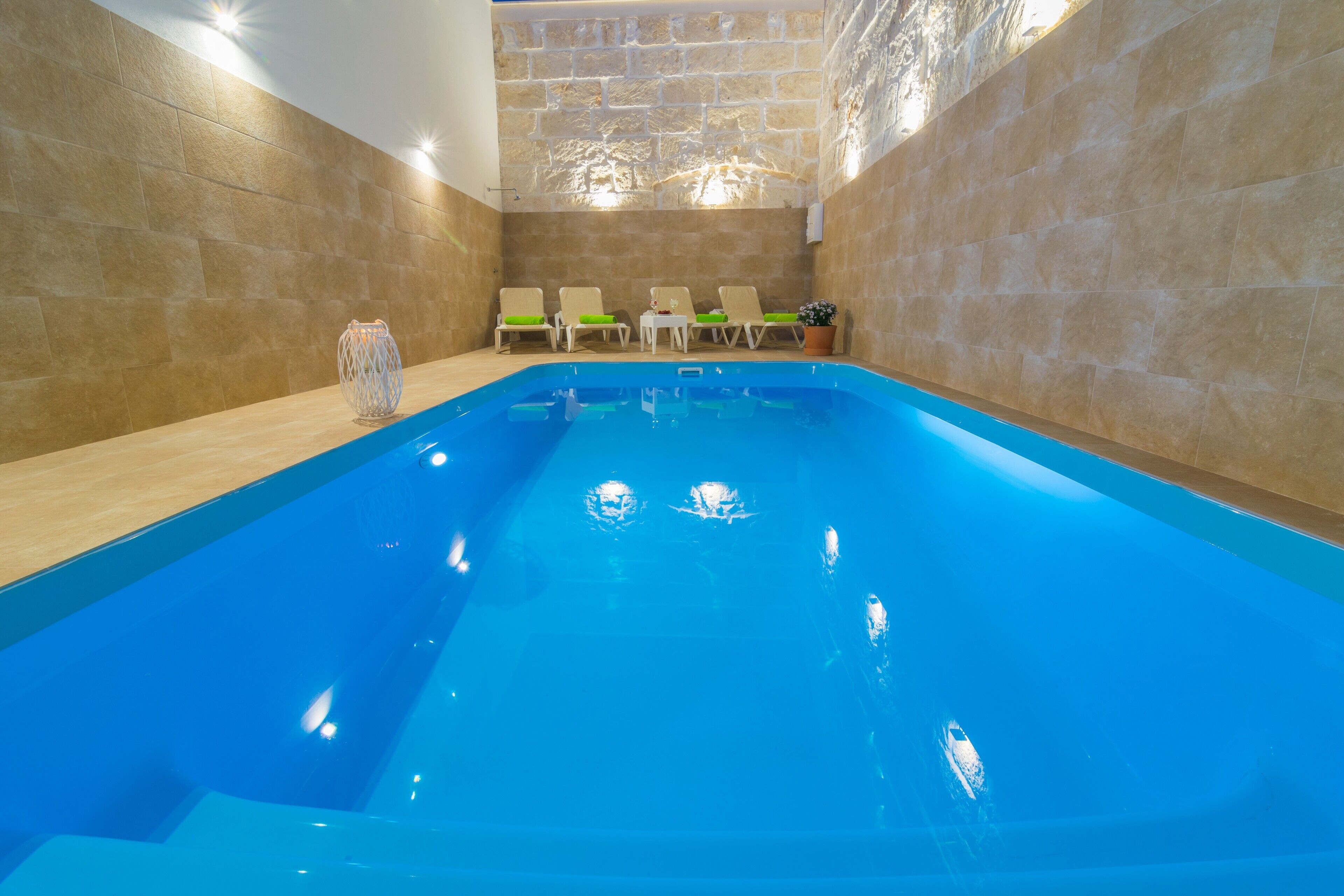 Una piscina interior con tres sillas de descanso y un jarrón decorativo.
