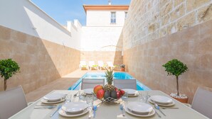 A dining area with a pool, white walls, and a view of a building in the background.