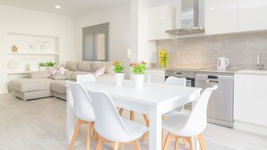 A modern kitchen with white cabinets, a stainless steel dishwasher, and a white dining table with chairs.