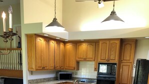 A kitchen with wooden cabinets, a granite countertop, a microwave, a stove, and a refrigerator. There is a dining area with a table and chairs. - Sunset View Estate, a farm setting, upscale house. (Cosby)