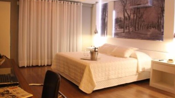 Una habitación de hotel con cama, escritorio, silla y un cuadro en la pared.