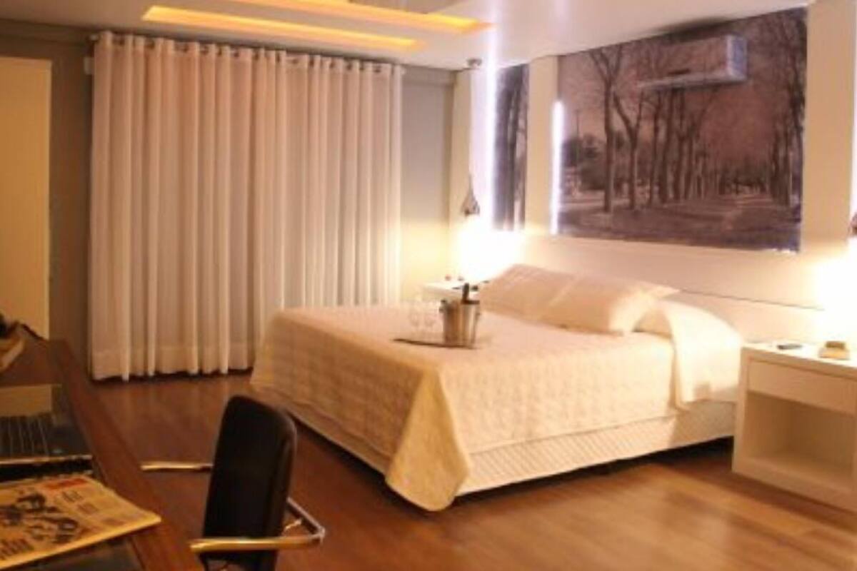 A hotel room with a bed, a desk, a chair, and a painting on the wall.