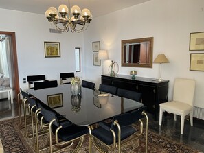 Une salle à manger avec une grande table noire, des chaises noires à cadre doré, un lustre et un miroir au mur.