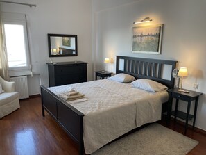 Une chambre à coucher bien rangée, avec un lit, des tables de chevet, une commode, un miroir et un tableau accroché au mur.
