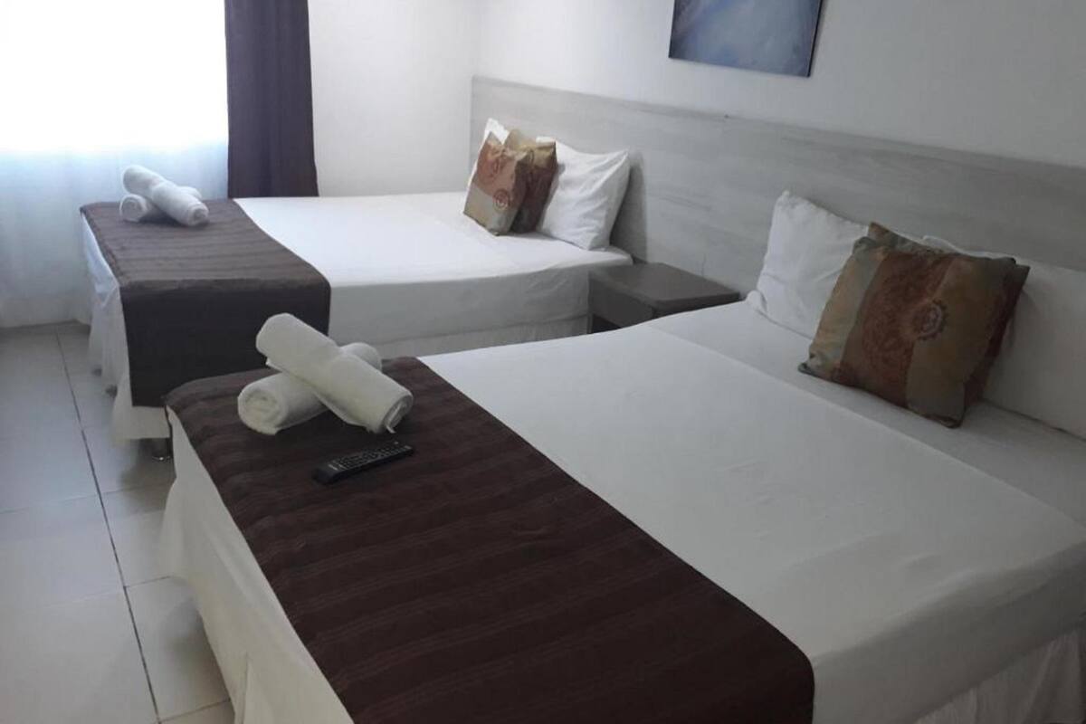 A hotel room with two beds, each with a brown headboard, white bedding, and a remote control on the bed.