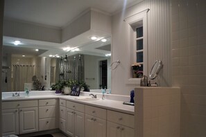 A modern bathroom with a large mirror, two sinks, and a shower area.