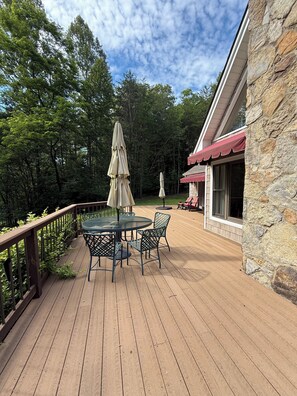 A wooden deck with a table and chairs, surrounded by a stone wall and a red awning.