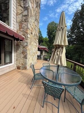 A deck with a round glass table and chairs, a beige umbrella, and a stone wall.