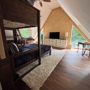 A loft bedroom with a bunk bed, a TV, a dresser, and a large window.