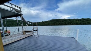 A wooden deck with a metal ladder and a chair, overlooking a calm lake with a forested shore. - NORRIS LAKE FRONT RENTALS : CAMP RUN A MUK-LAKE FRONT with PRIVATE DOCK (Lafollette)