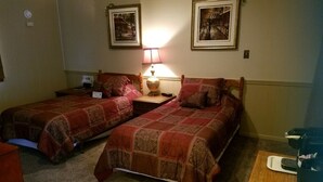 Une chambre d’hôtel avec deux lits simples, une table de chevet avec une lampe, une petite table avec un plateau, et des tableaux encadrés au mur.