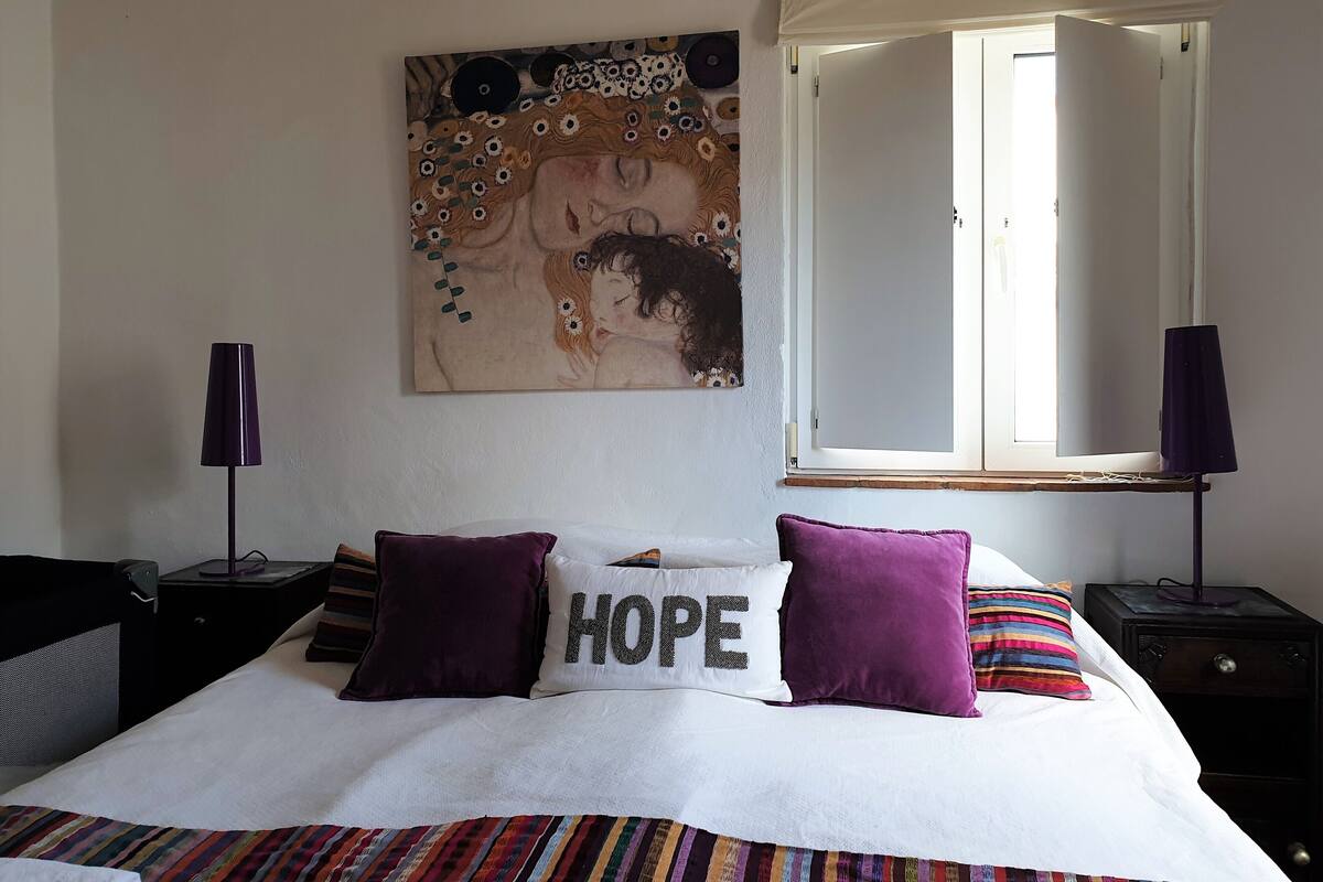 A bedroom with a bed, a window, a painting, and two nightstands.
