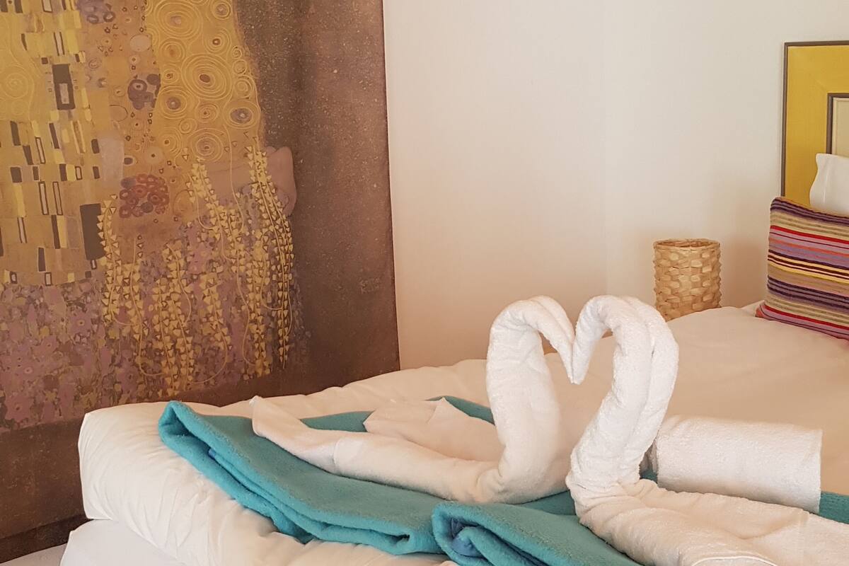 A hotel room with a bed, a painting on the wall, and a swan-shaped towel arrangement.
