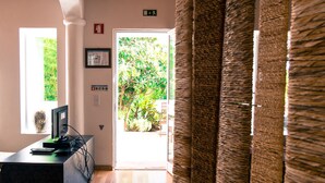 A hallway with a wooden desk, a computer, and a window with a view of greenery. There is a door with a sign above it and a wall-mounted light switch. - Quinta dos Cochichos – Country Houses (Olhao)