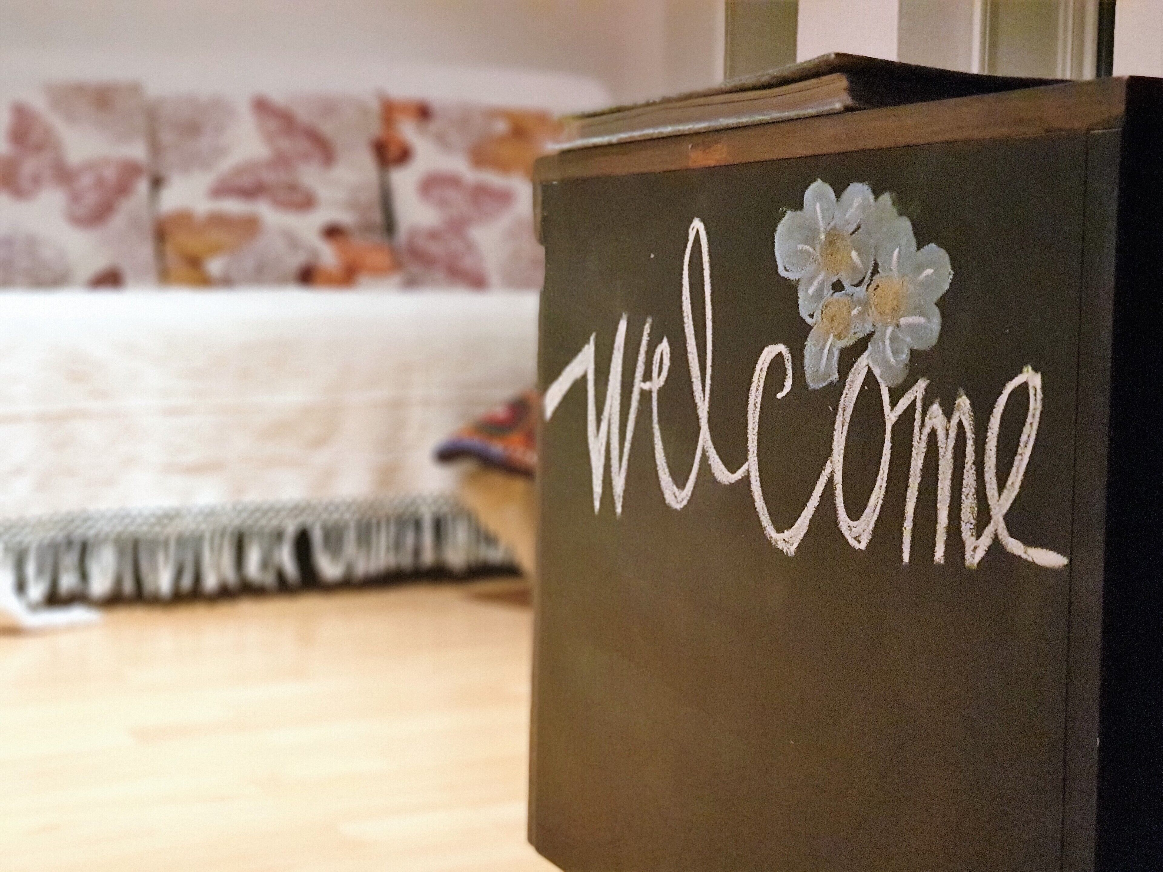Eine Holzkiste mit der Aufschrift 'welcome' und einer Blumenverzierung.