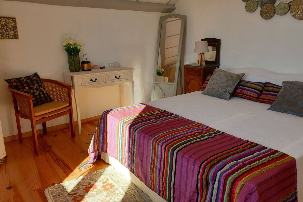 A bedroom with a bed, a chair, a dresser, a mirror, and a wall decoration.