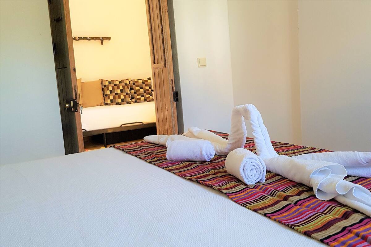 A hotel room with a bed, a striped rug, and towels arranged on the bed.